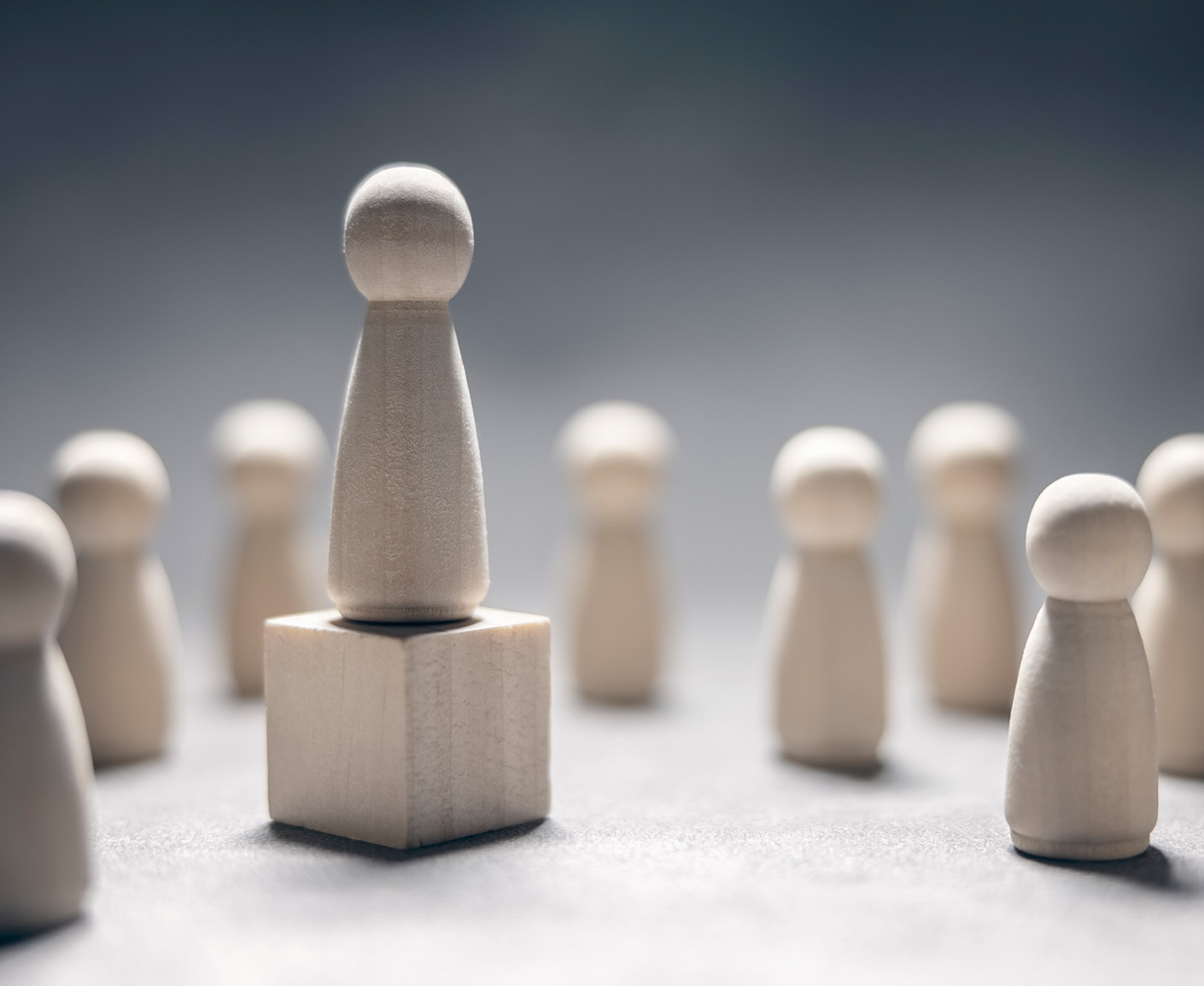 Grey-white wooden pawn standing on a cube, addressing a group of pawns arranged around it.